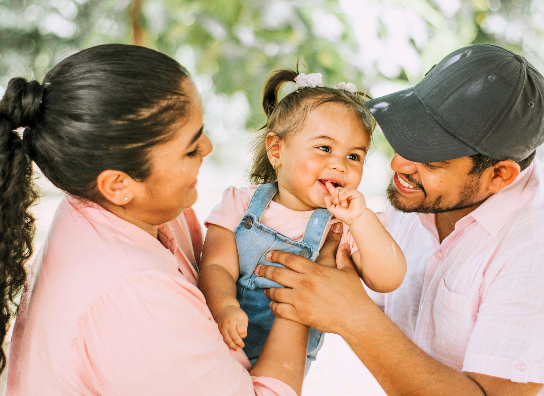 Hispanic family of three holding up their little girl.