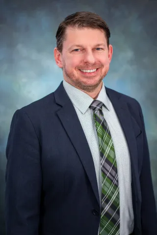 Richard Moore's headshot. He is wearing a navy suit and plaid tie while smiling at the camera.