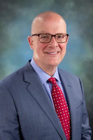 Tim Van Zandt's headshot. He is wearing a suit and tie with rectangular glasses and smiling at the camera.